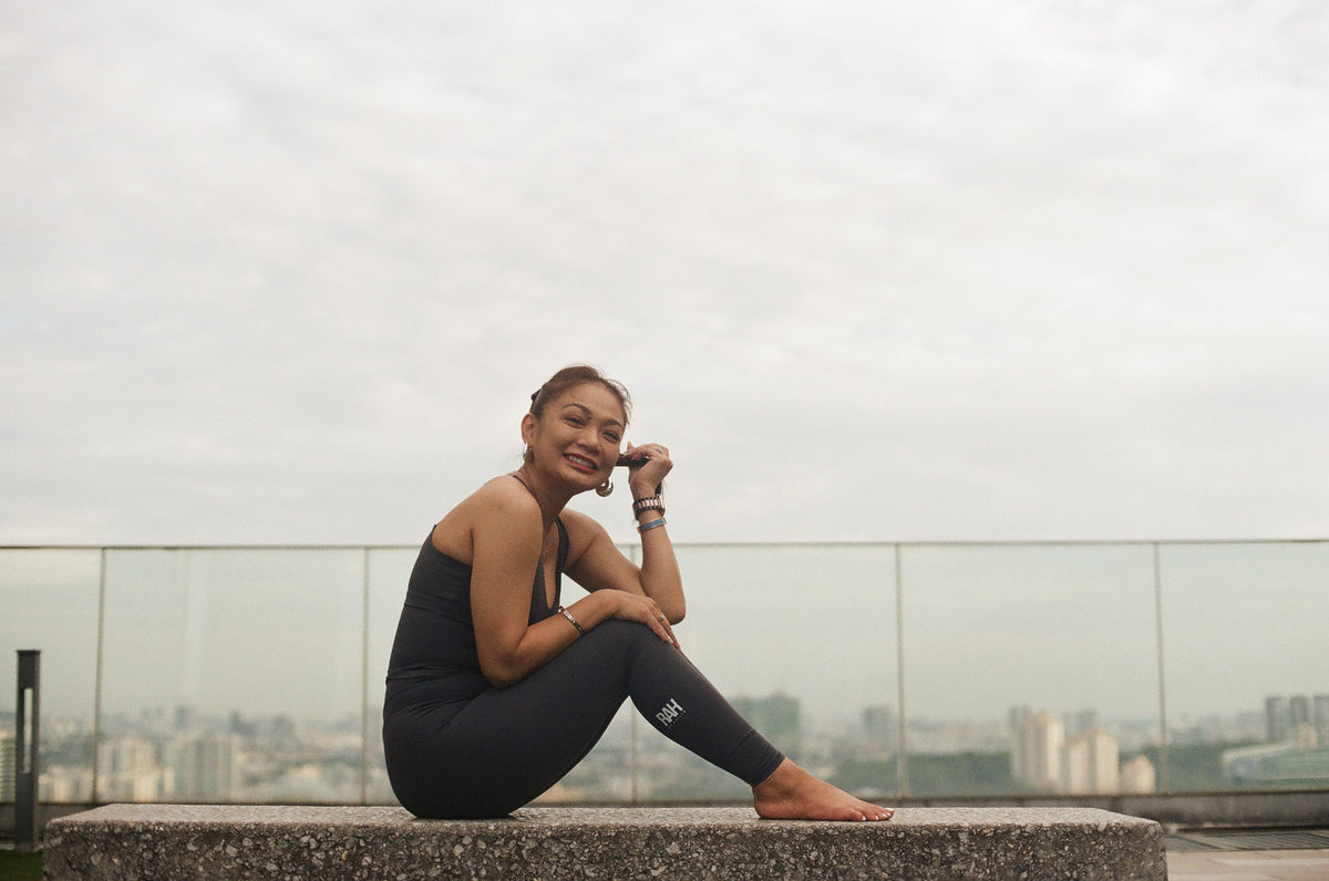 EQL x RAH longline sports bra in Blue Grey, seated on a rooftop ledge